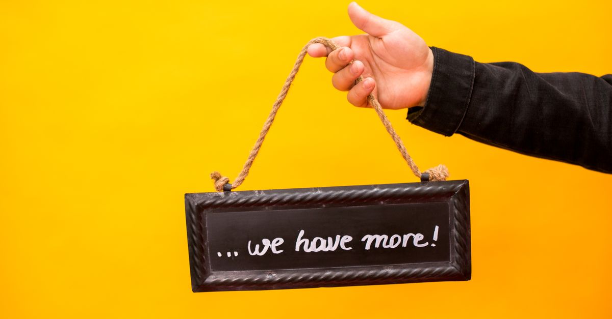 A hand holding a sign that reads 'we have more' against a yellow background.