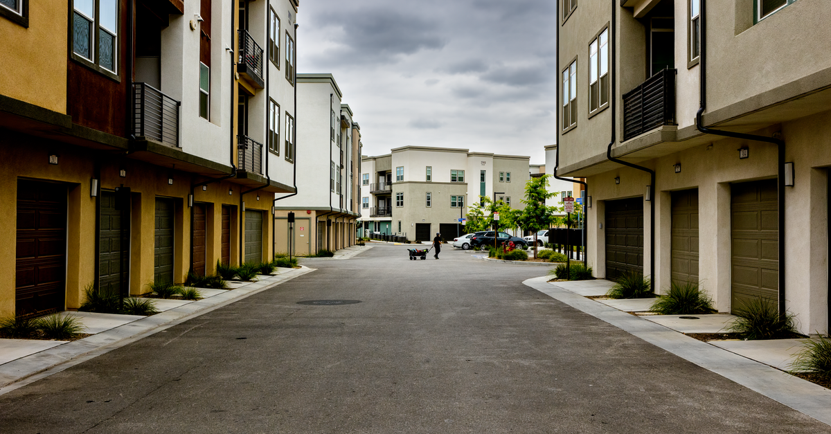 A man pulls a cart down a quiet residential street lined with modern townhouses.