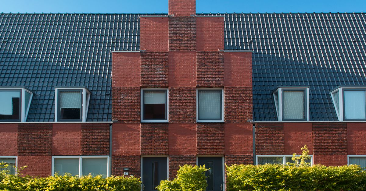 Contemporary brick townhouse facade with neat hedge under clear blue sky.