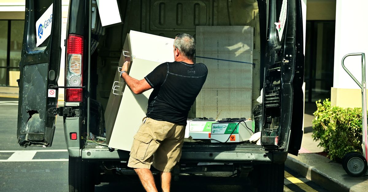 Adult man loading furniture into an open van in a parking lot, daytime setting.