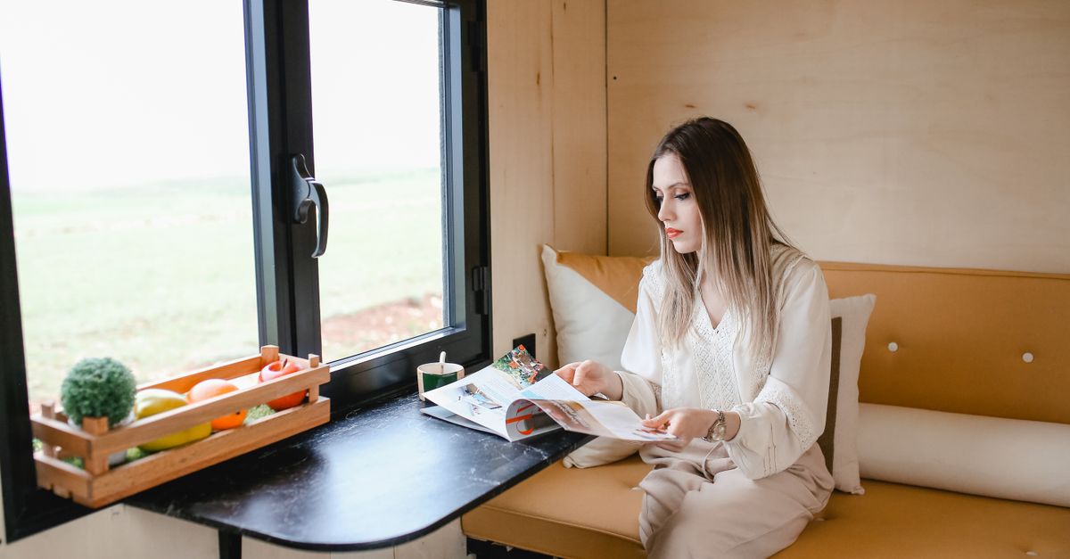 Woman reading magazine in a cozy tiny house with a scenic view.