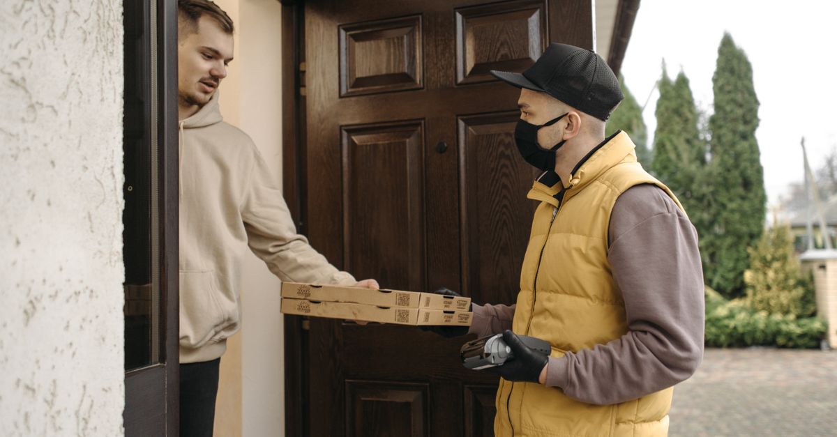 Courier delivering pizza boxes at the doorstep using contactless payment method.