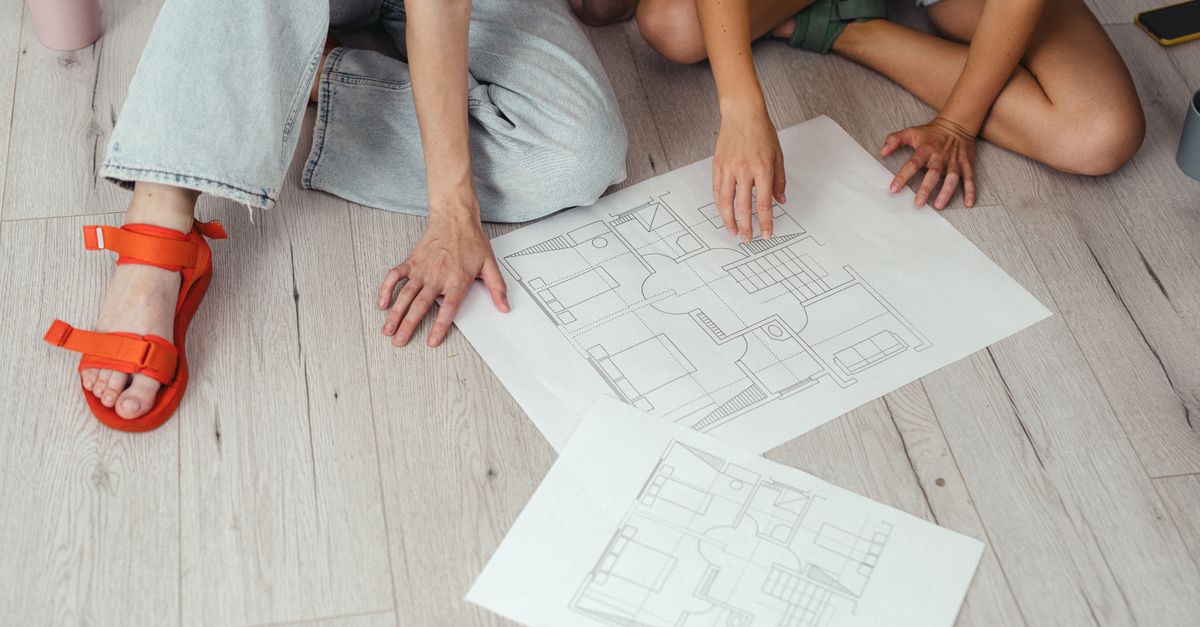 Two people discussing house blueprints on a light wooden floor.