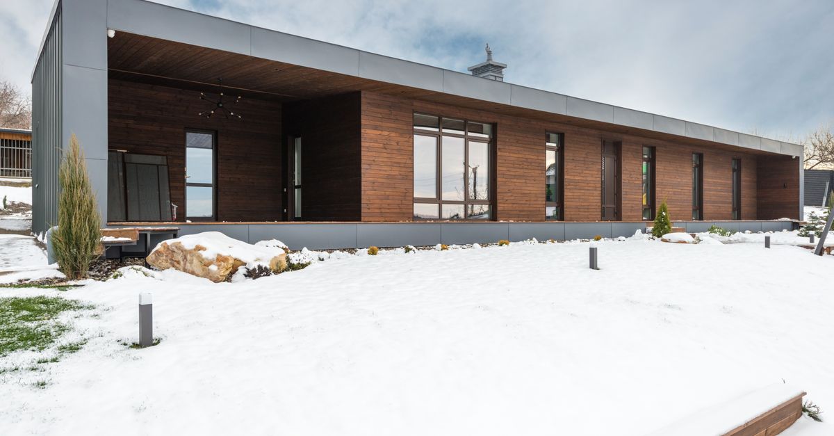 A sleek modern wooden house stands surrounded by a snowy winter landscape, showcasing contemporary architecture.
