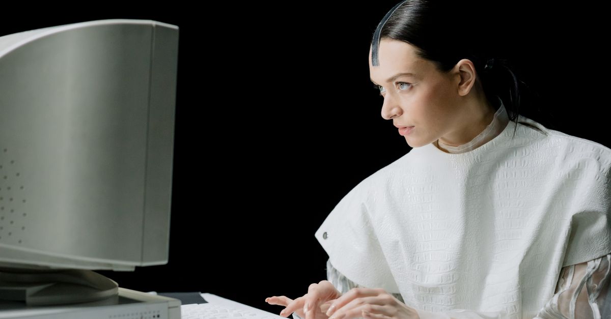 A woman in futuristic attire types on a vintage computer, blending old and new technology.