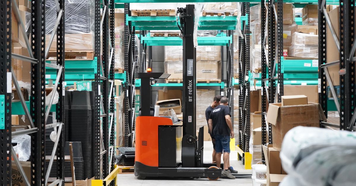 Warehouse scene featuring workers and a forklift navigating aisles for logistics and inventory management.