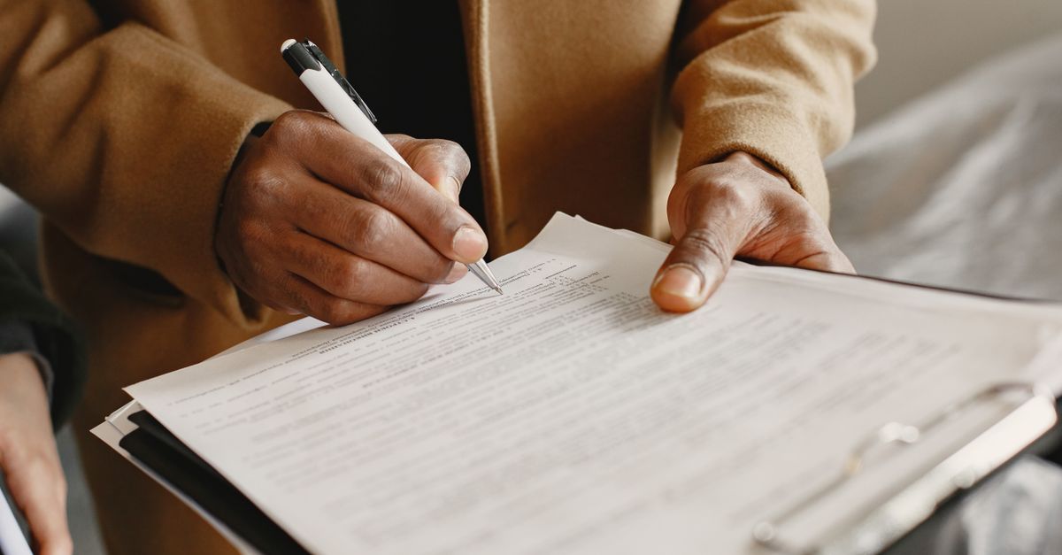 Close-up of a person signing a contract on a clipboard, focusing on legal formalities.