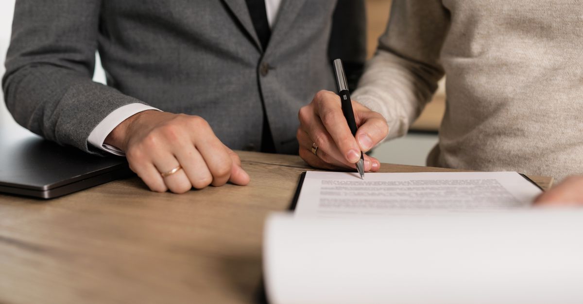 Close-up of businessmen signing documents at a wooden table in an office.