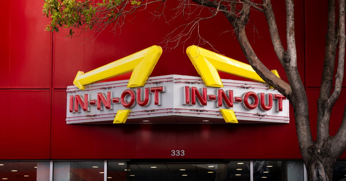 Iconic In-N-Out Burger sign with bold red background and trees in the foreground.