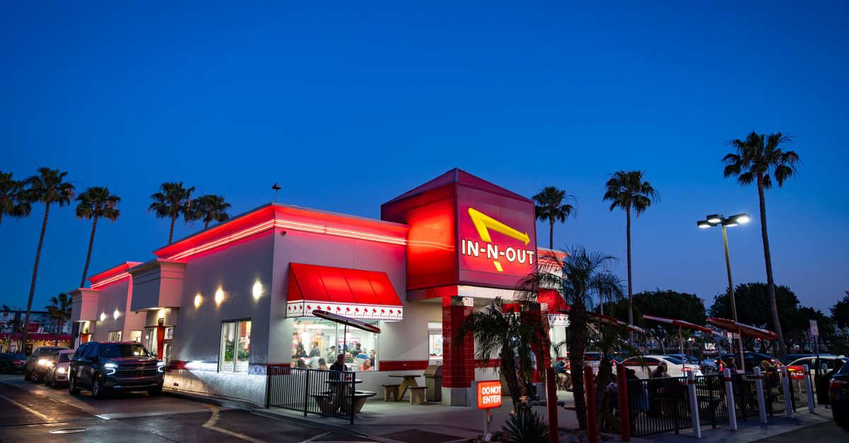 Vibrant In-N-Out Burger fast-food restaurant captured during twilight with palm trees around.