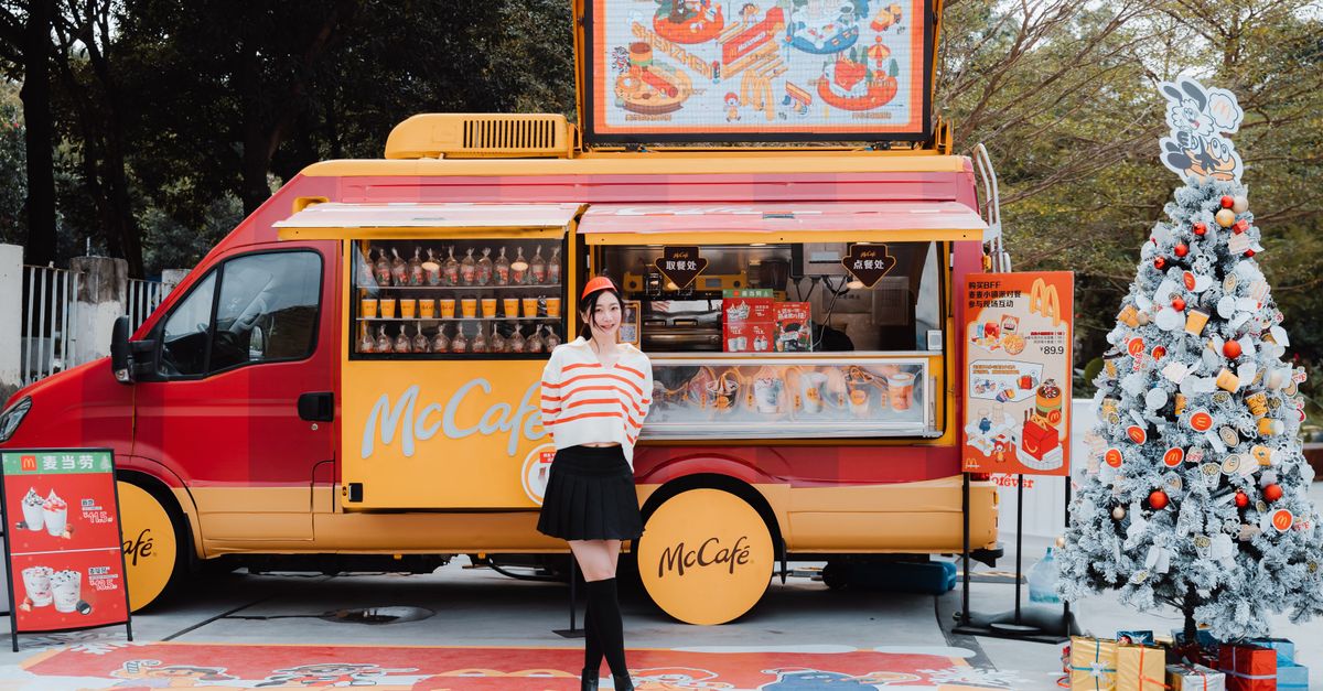 Woman standing by a McCafe food truck with Christmas decorations, creating a festive urban atmosphere.
