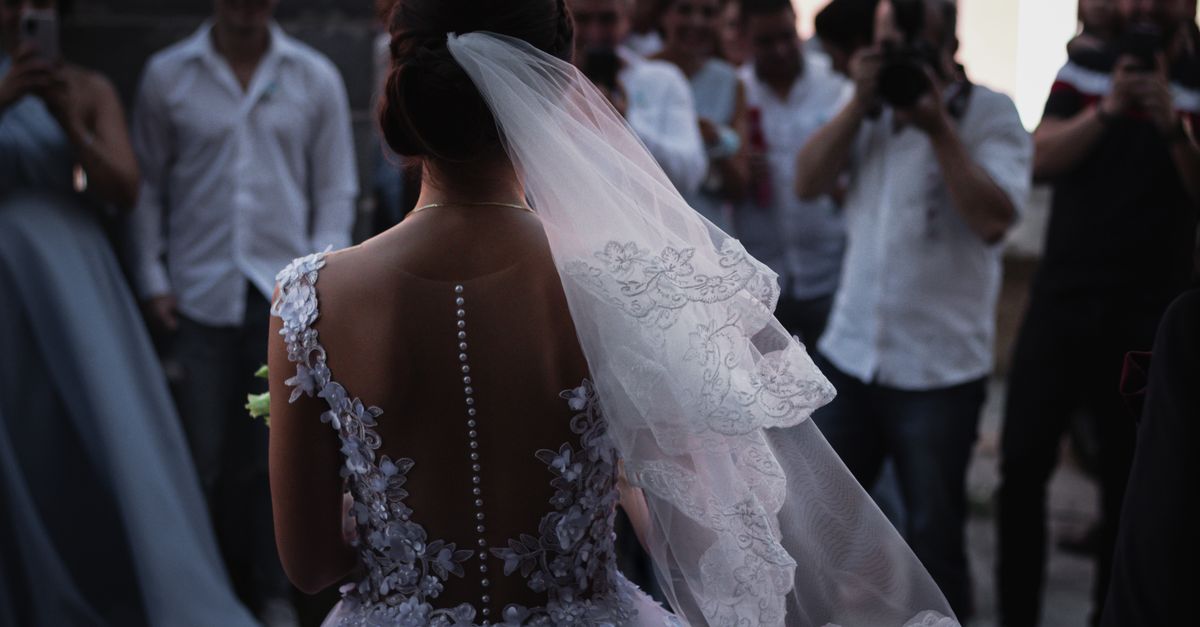 A bride in a white lace dress stands before a crowd at her wedding ceremony, creating a romantic moment.