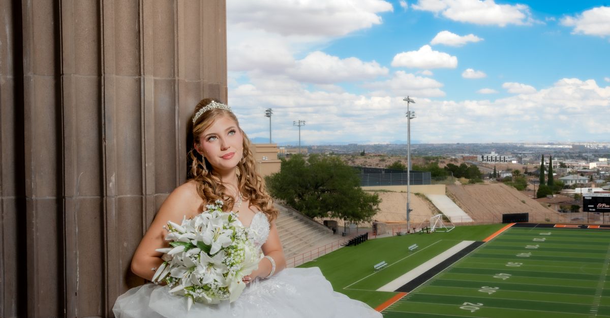 A bride in a white gown holds a bouquet with a scenic stadium and city view in the background.