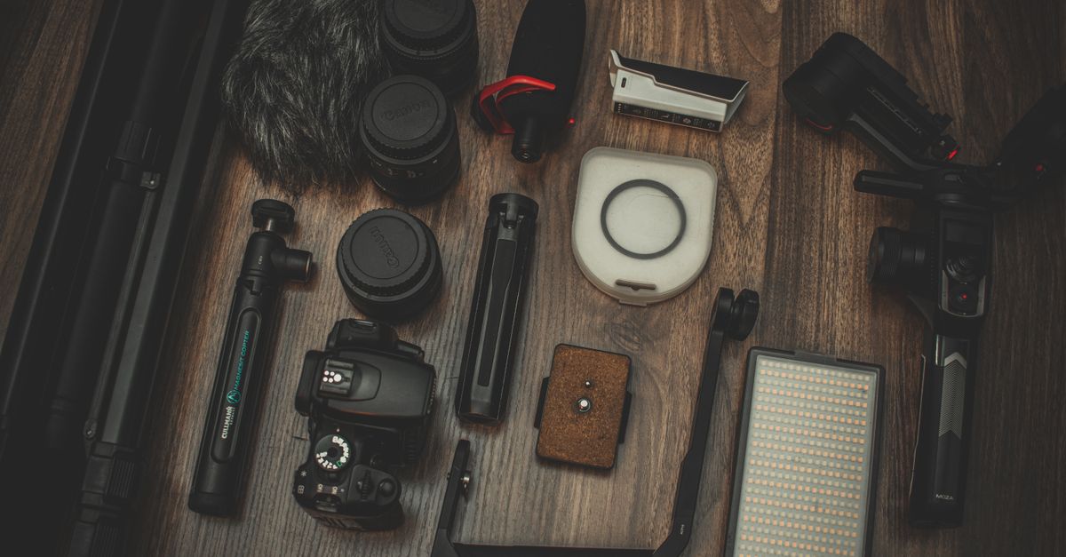 A collection of professional photography gear including a DSLR camera, lenses, and microphone arranged on a wooden surface.