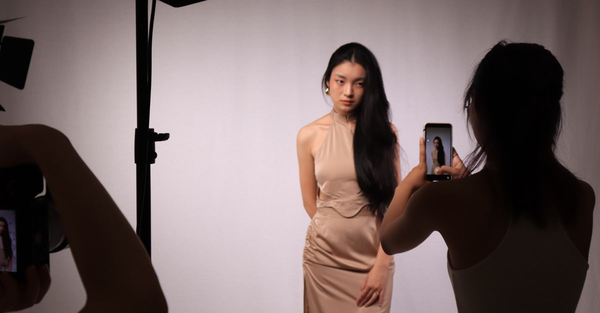 A professional studio photoshoot capturing a woman in a beige dress, using digital cameras and smartphones.