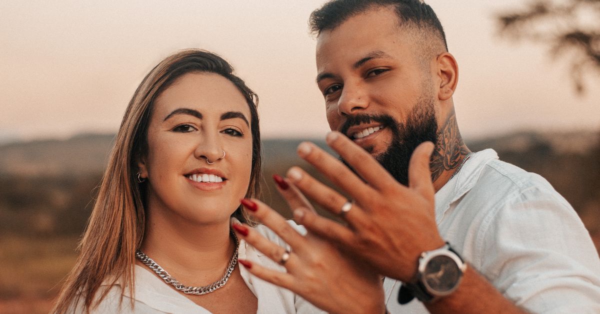 Smiling couple joyfully displaying their engagement rings in an outdoor setting.