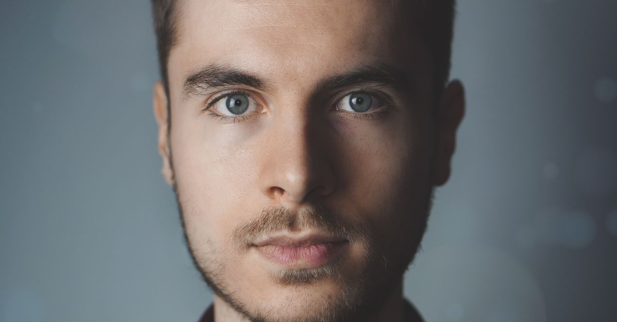 Close-up portrait of a young man with facial hair and a serious expression.