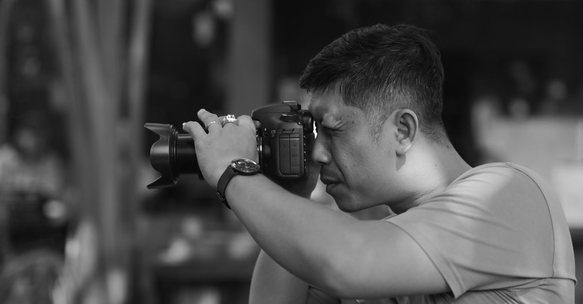 Black and white profile of a photographer using a DSLR camera outdoors.