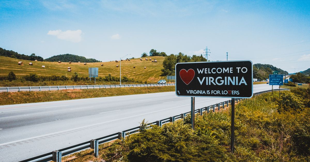 Empty asphalt highway in hilly countryside near road sign with welcome to Virginia inscription on sunny day
