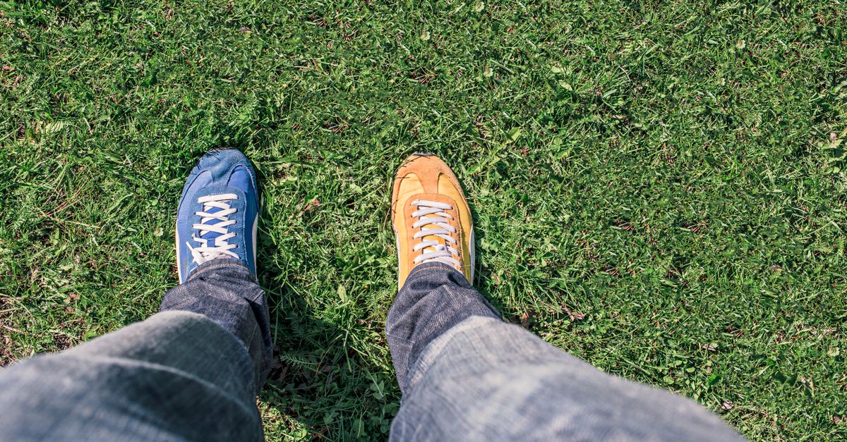 A person wearing mismatched shoes stands on green grass, highlighting differences and individuality.