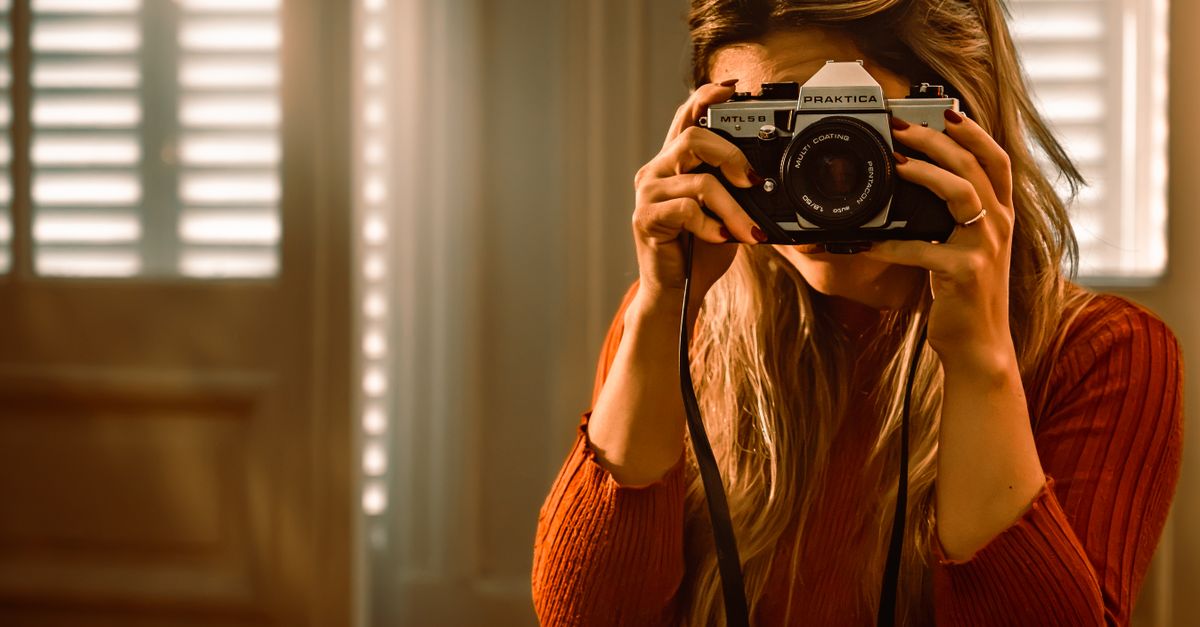 A young woman with sunglasses holds a vintage camera indoors, capturing a cozy moment.