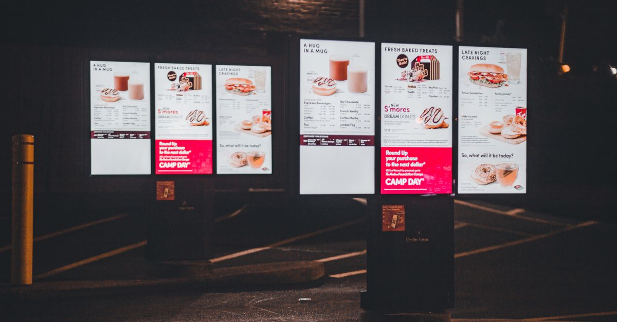 Nighttime view of an illuminated fast food drive-thru menu with digital display and clear copyspace.
