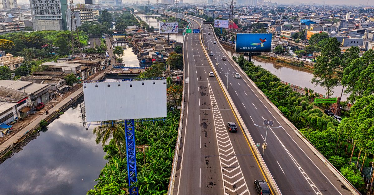 Dynamic aerial view of an expressway in Jakarta cityscape with skyline and river in sight.