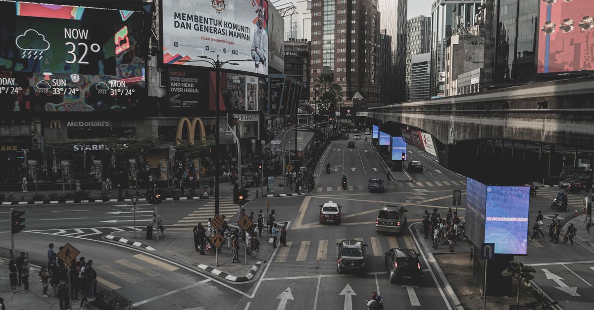 City street view of Kuala Lumpur showcasing traffic and billboards under a cloudy sky.