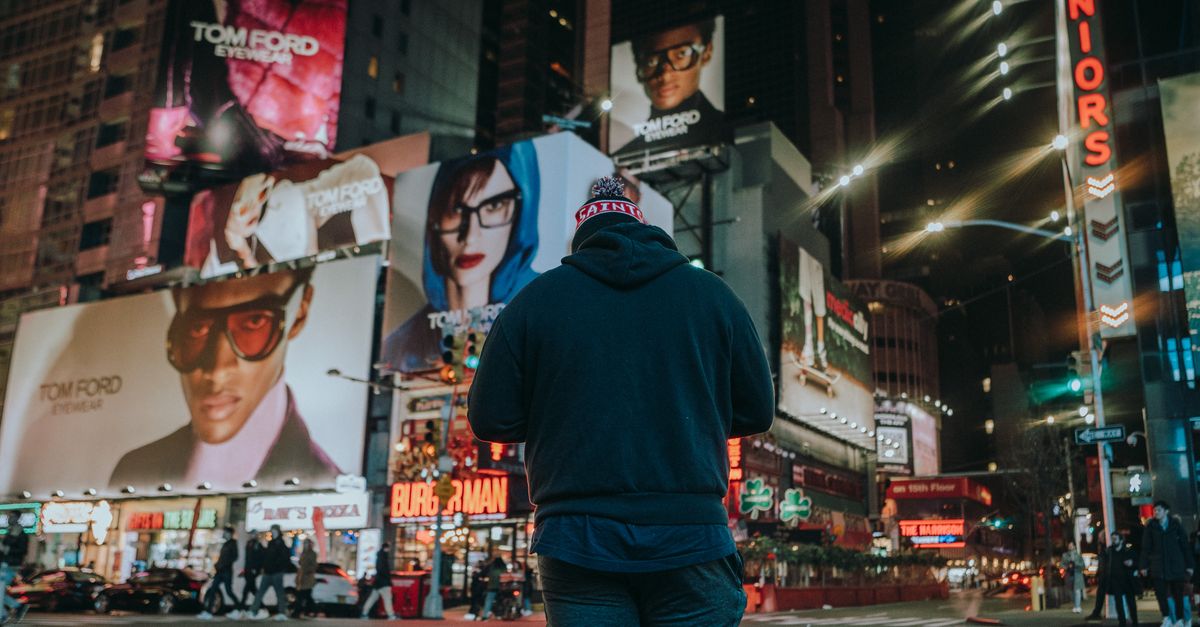 Street scene with a man standing in a vibrant city at night, surrounded by billboards.