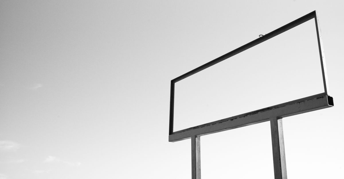 A solitary, empty billboard stands in a rural landscape under a clear sky.