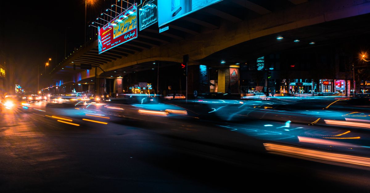 Long exposure of a bustling urban roadway at night with striking light trails and illuminated billboards.
