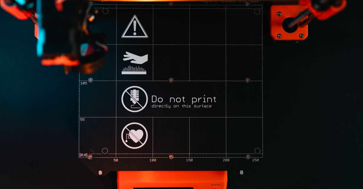 3D printer build plate with warning symbols, showcasing high-tech equipment in a workspace.