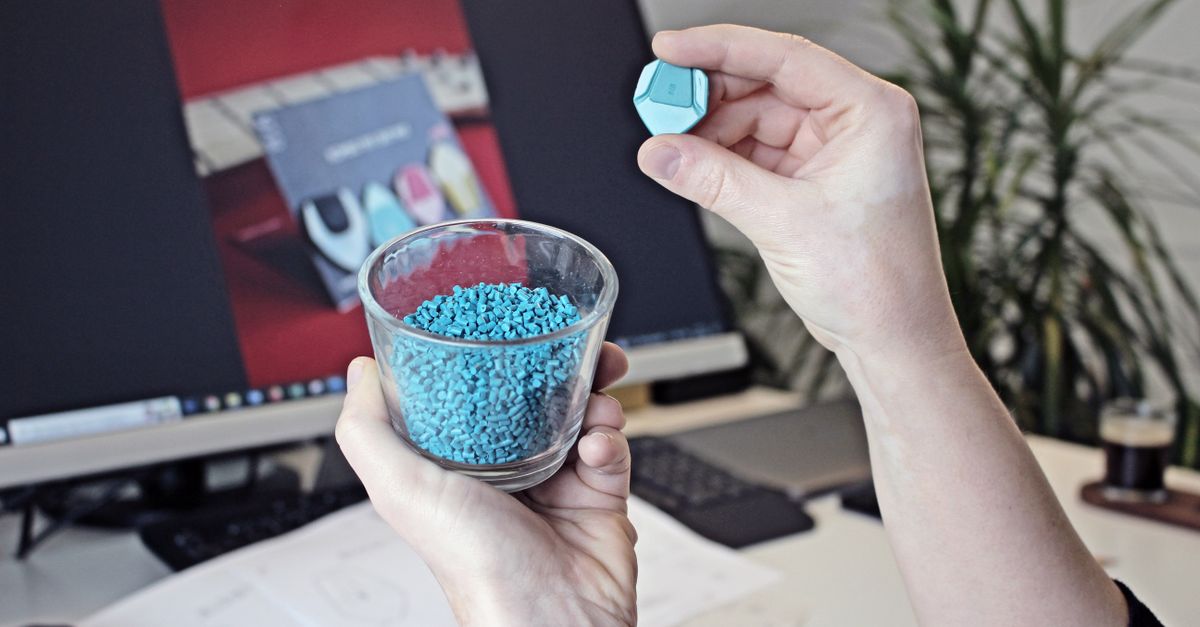 Hands holding plastic granules with a computer screen in the background, showcasing 3D printing materials.