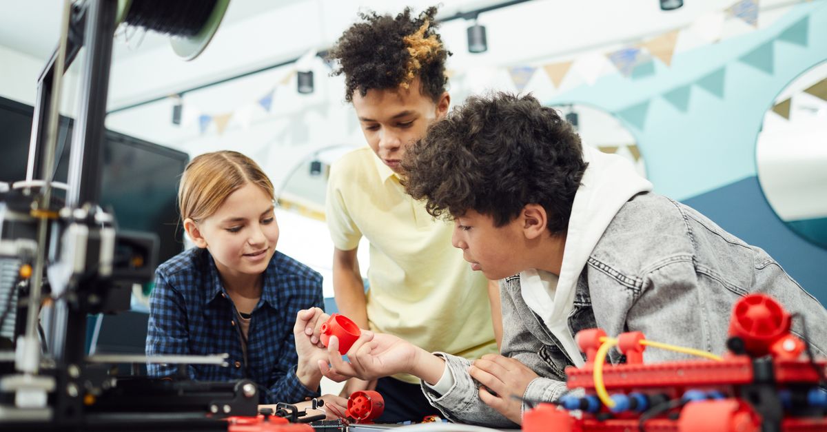 Concentrated group of children sitting at table and exploring new engineering device together in light room