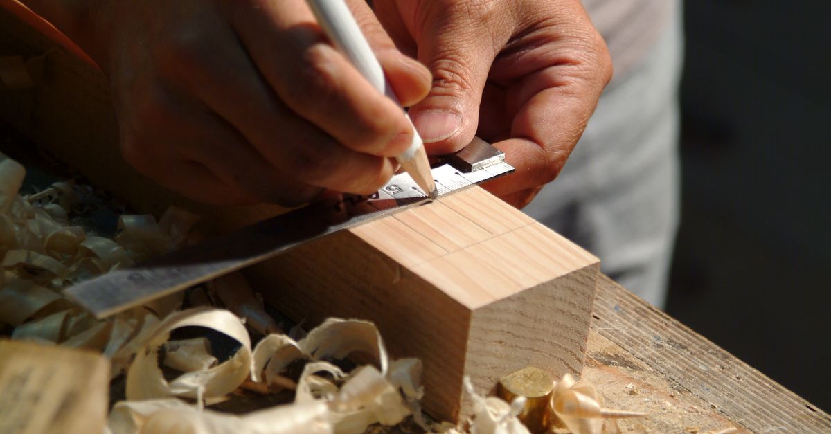 Close-up of hands measuring a wooden plank using a ruler and pencil on a workbench.