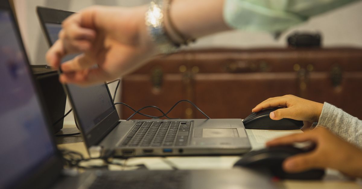Crop anonymous female teacher pointing at netbook screen near schoolchildren touching mouses at desk in classroom