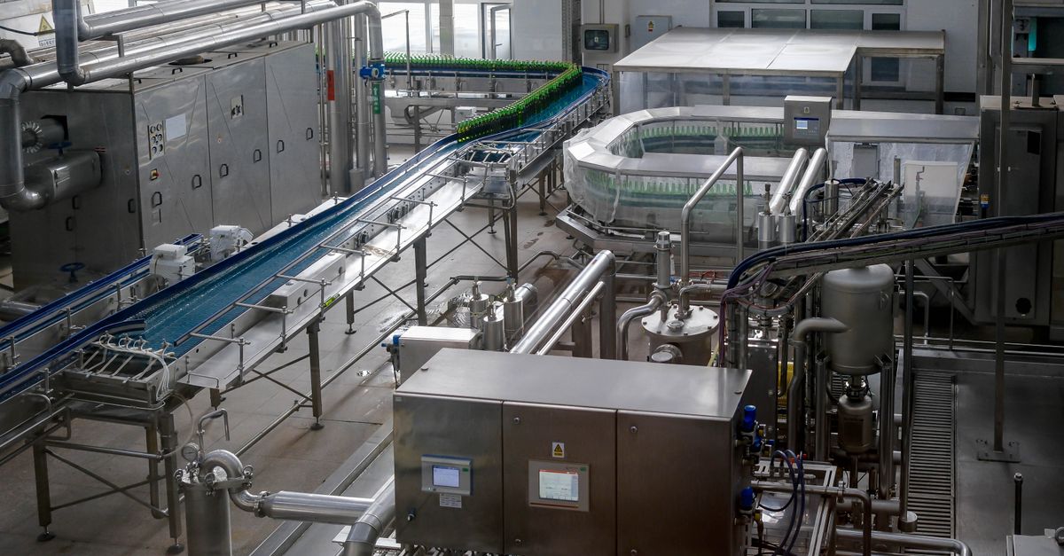 Interior view of an automated beverage bottling factory with machinery and conveyor belts.