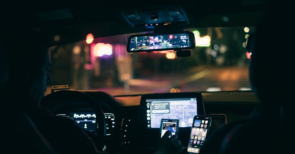 Interior view of a car at night with a driver using a smartphone for navigation through city streets.