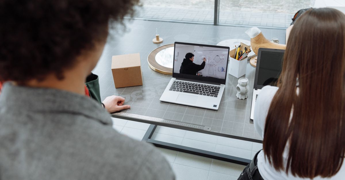 Two colleagues engaging in a remote online meeting at a desk with a laptop.