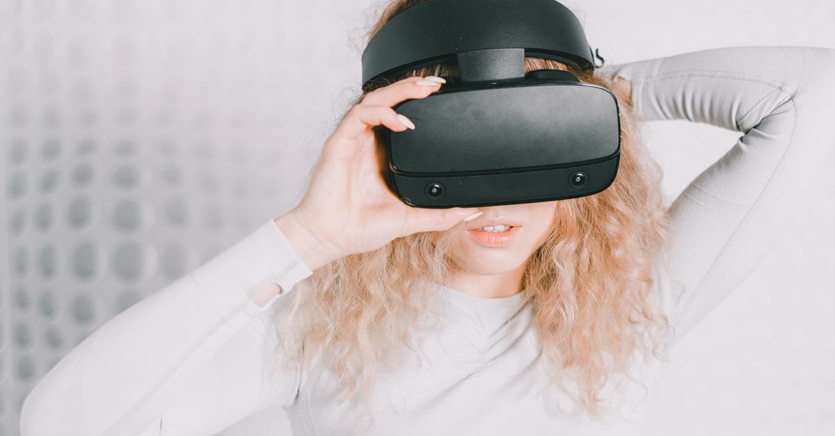 Blonde woman using a VR headset exploring virtual reality indoors.
