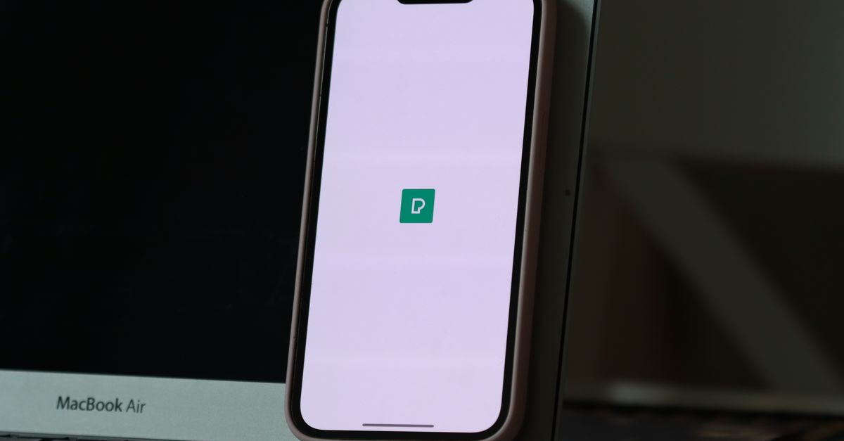 Smartphone resting against a laptop screen with app icon displayed, indoors.