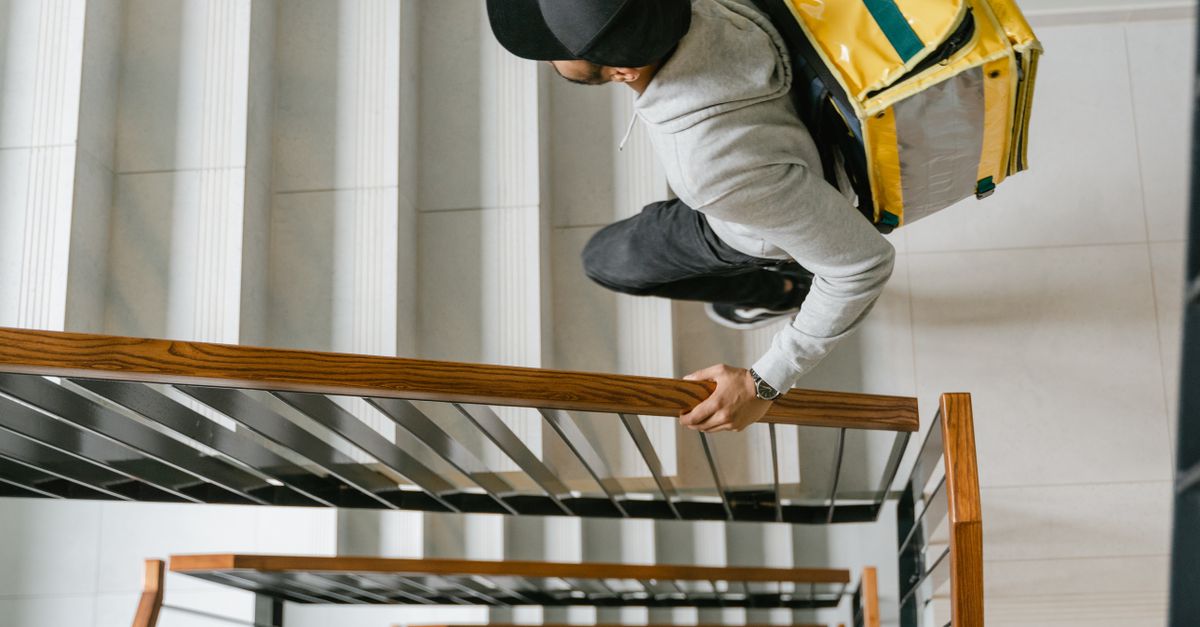 Food delivery person climbing stairs with a thermal bag, seen from above in a modern building.