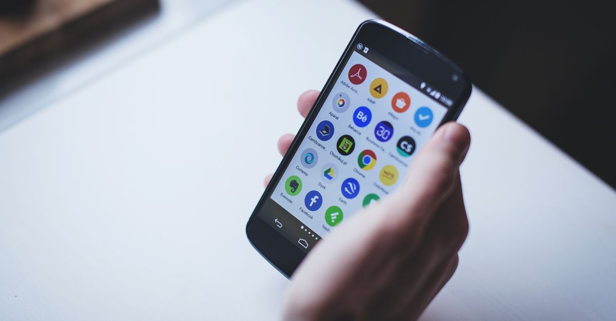 Close-up of a person holding a smartphone with various app icons visible on the screen.