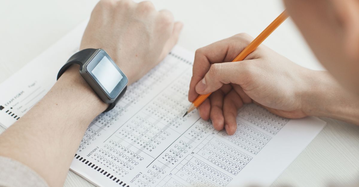 Close-up of a student writing answers on a test sheet with a pencil and smartwatch.