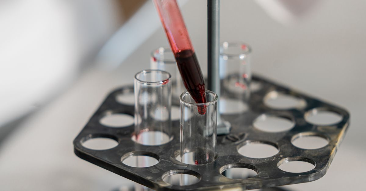 Red liquid being transferred into test tubes in a lab setting for research.