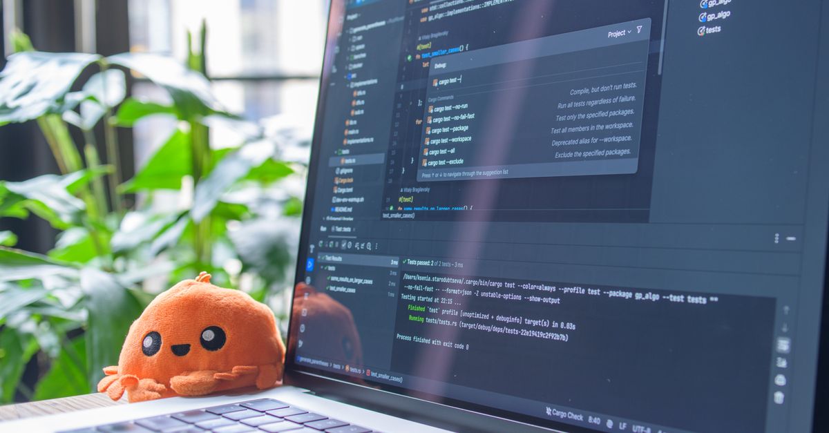 Open laptop with code editor displaying, next to an orange plush toy and green plants.