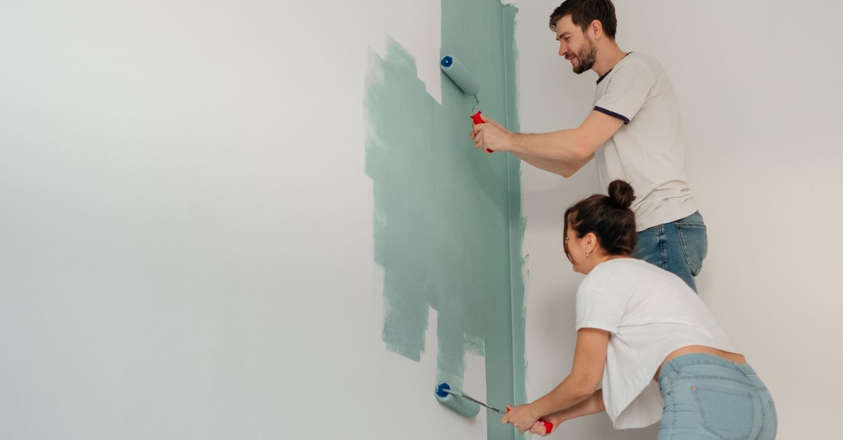A young couple collaborates on painting a wall with rollers, highlighting teamwork and home improvement.
