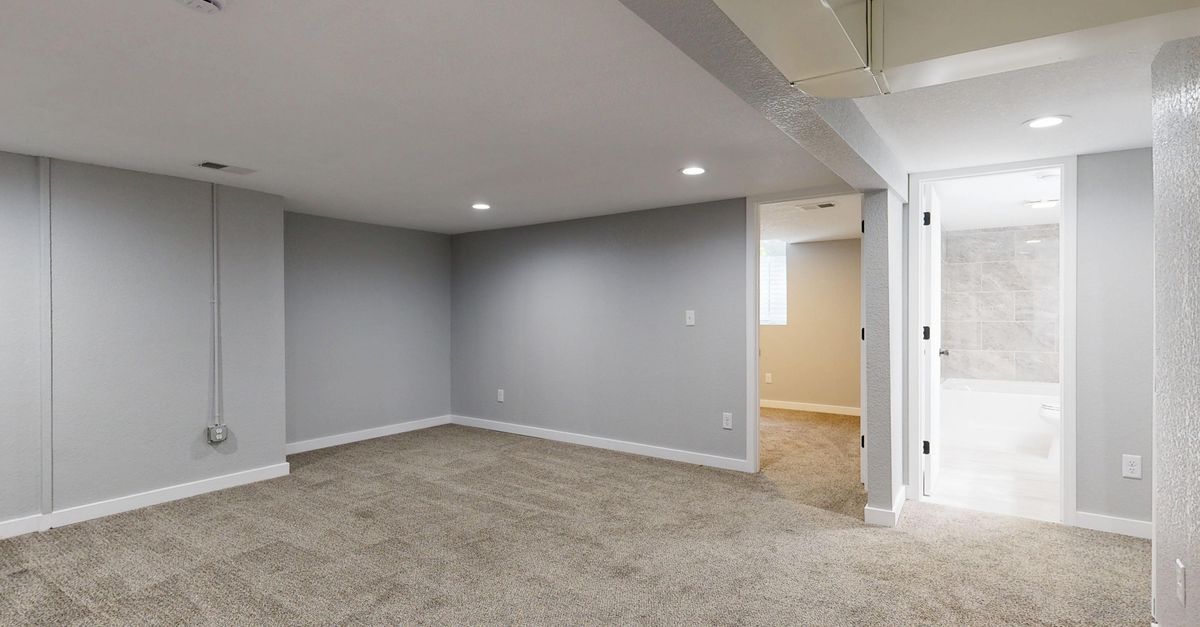 Empty basement room with neutral carpet and recessed lighting.