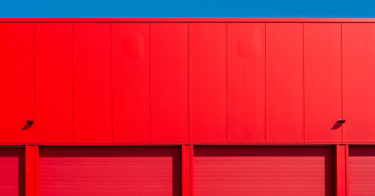 Bright red garage doors of an industrial building against a clear blue sky, showcasing minimalism.