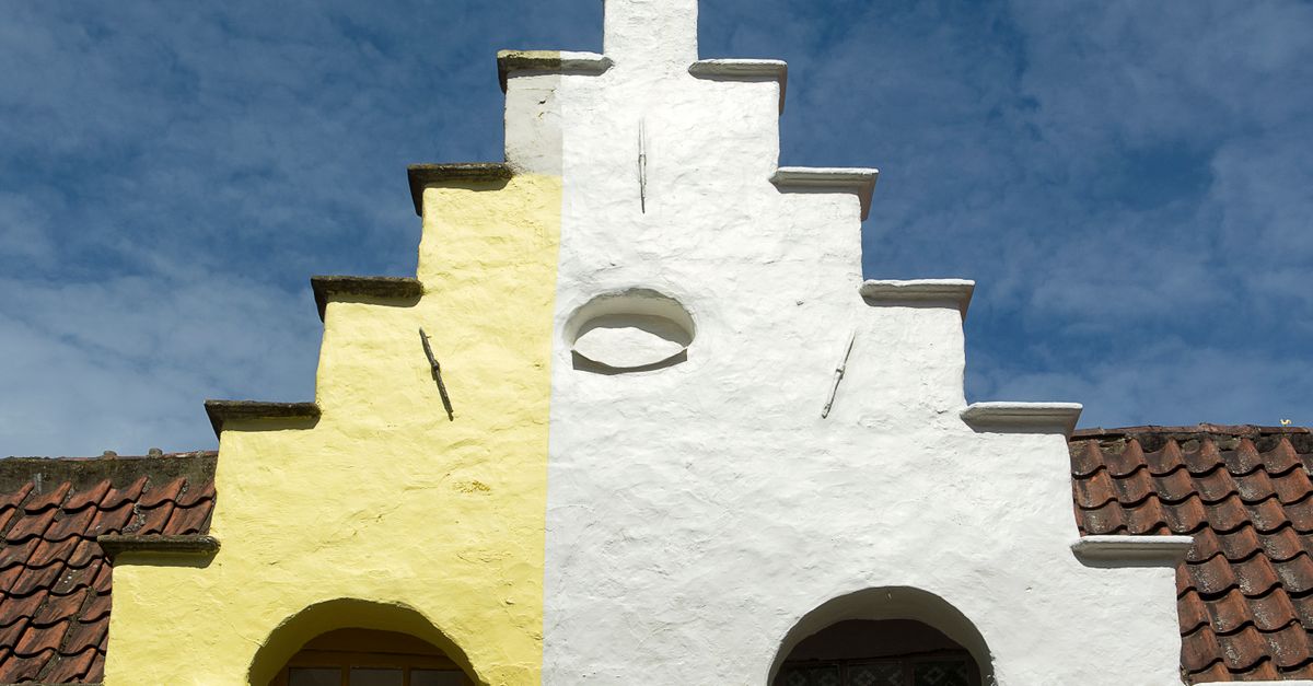 Colorful historic house facade with yellow and white paint under a clear blue sky. Architectural detail and style.